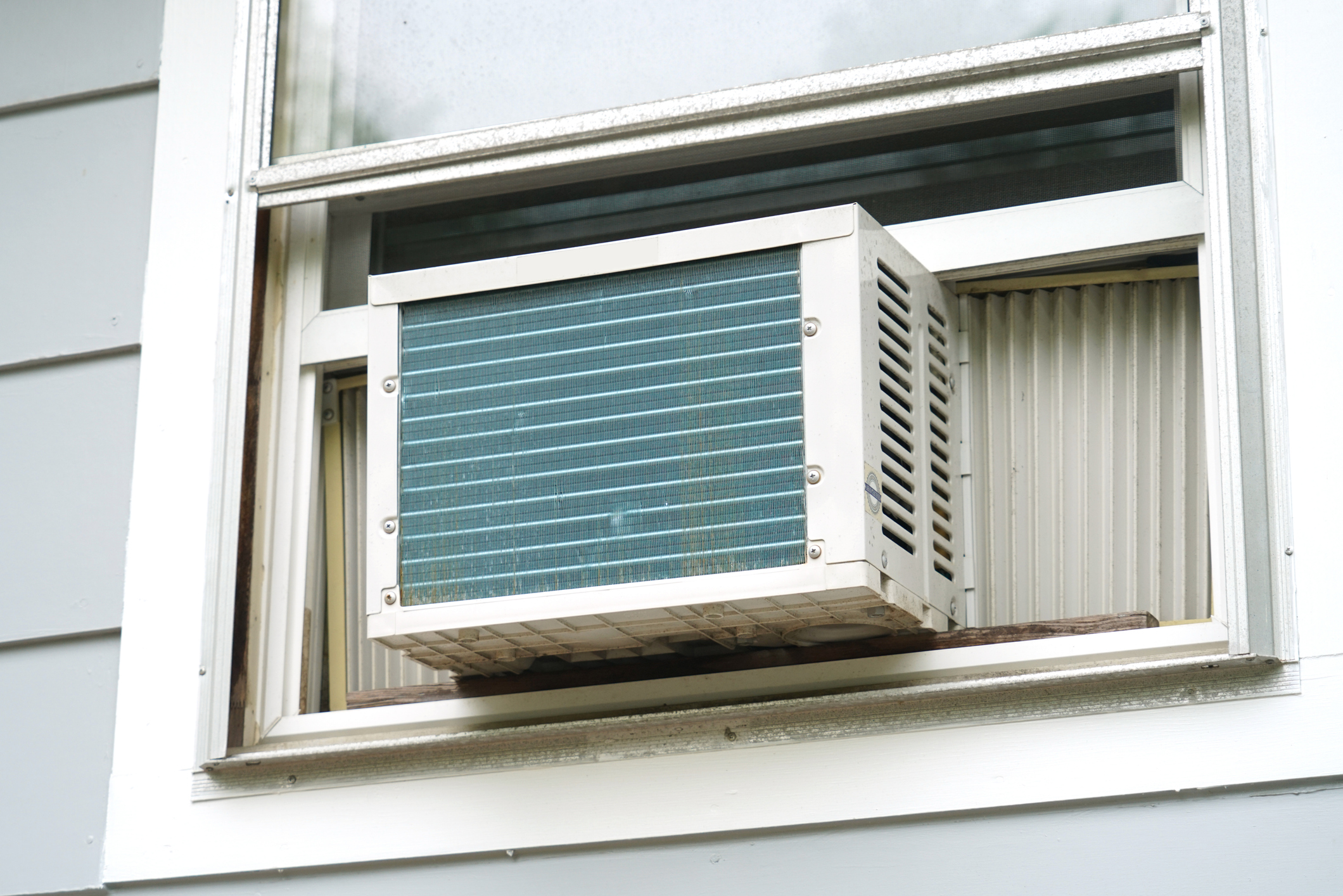 Exterior image of the back of a window AC unit installed in a white-framed double-hung window.