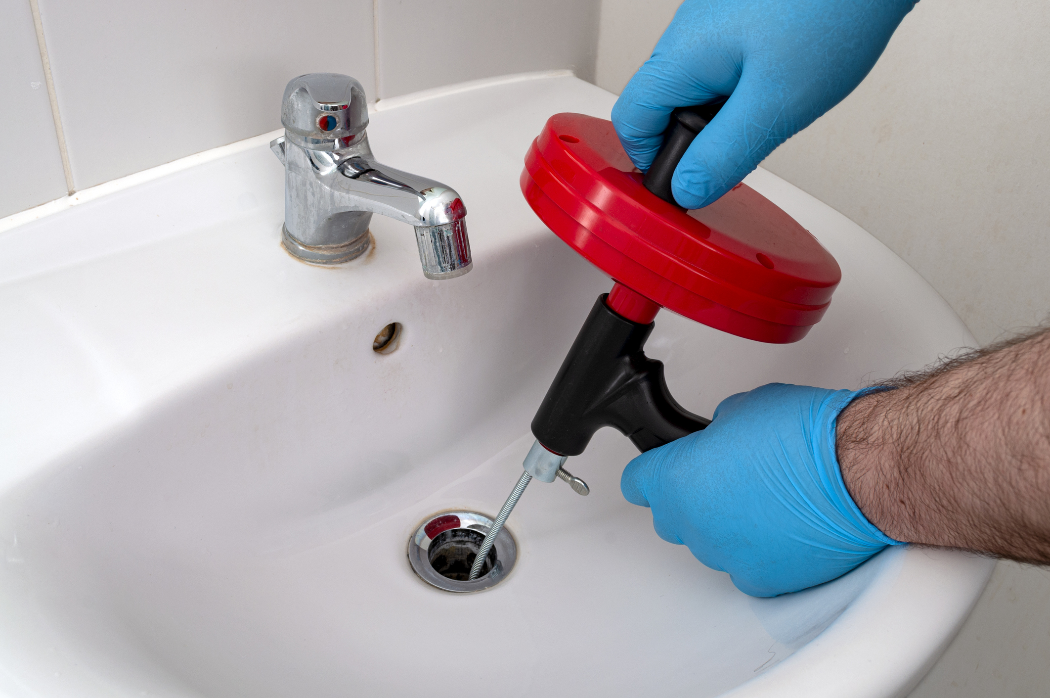 Plumber with blue gloves using drain snake in bathroom sink